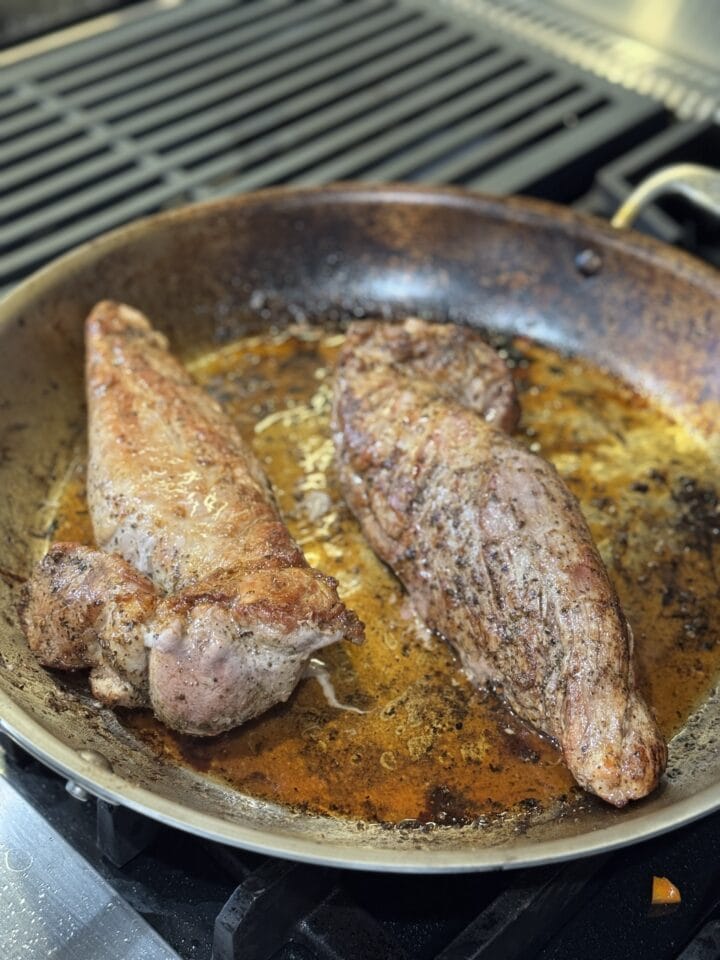 a photo of two pork loins seared in a pan
