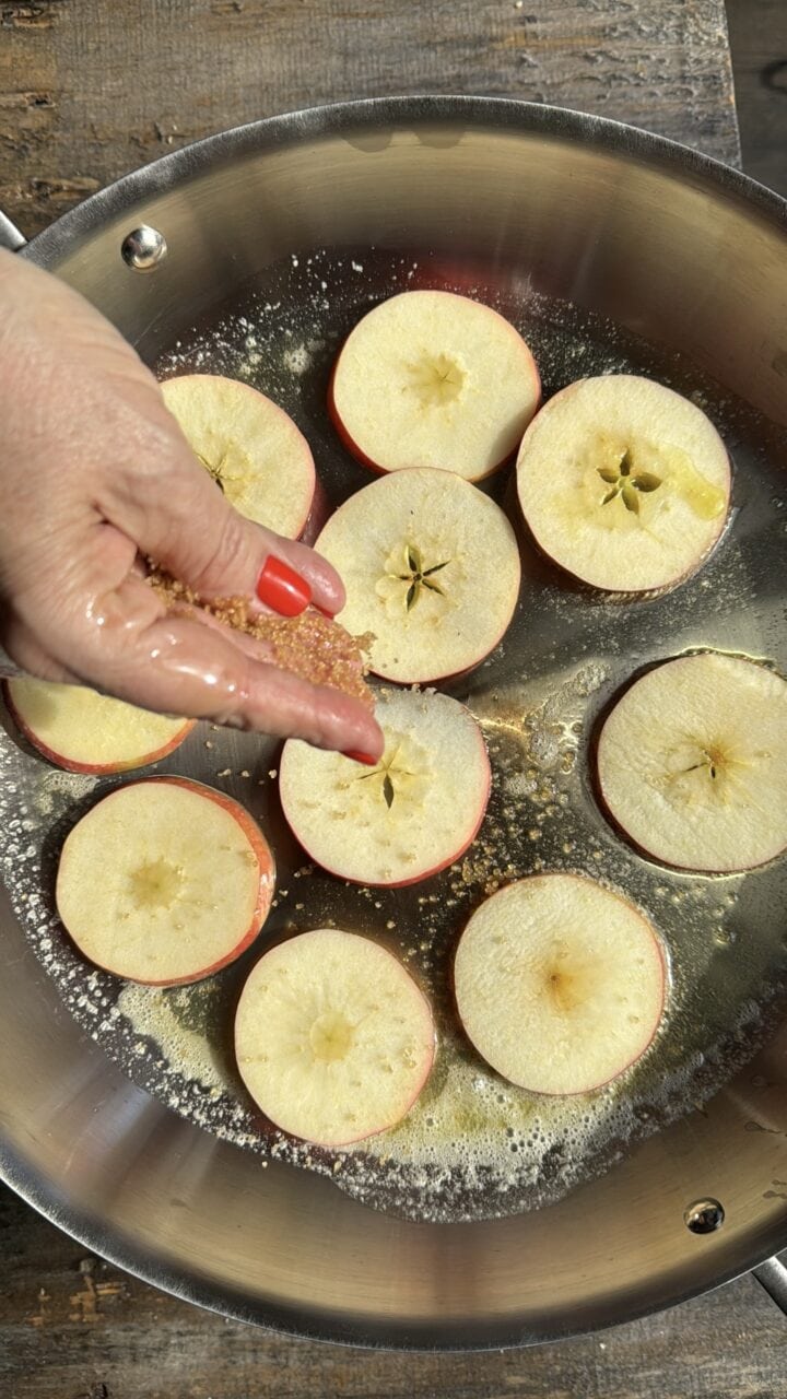 Sliced apples being seasoned in a stainless steel pan, preparing for cooking or baking.