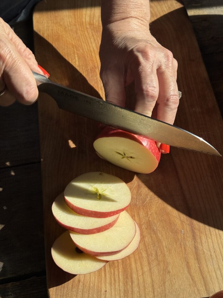 Crisp red apple being sliced on a wooden cutting board, fresh healthy snack for cooking or baking.