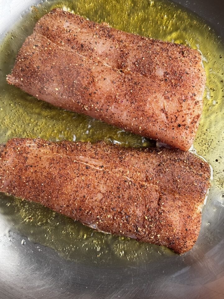 fish covered in a spice blend in a stainless steel pan with oil