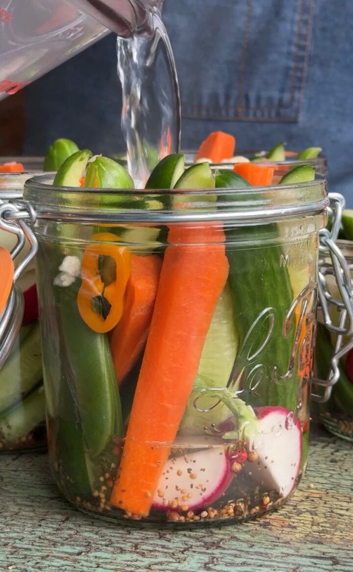 pouring brine onto refrigerator pickles in a jar