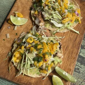 two fish tacos with mango salsa on a wooden cutting board with lime wedges