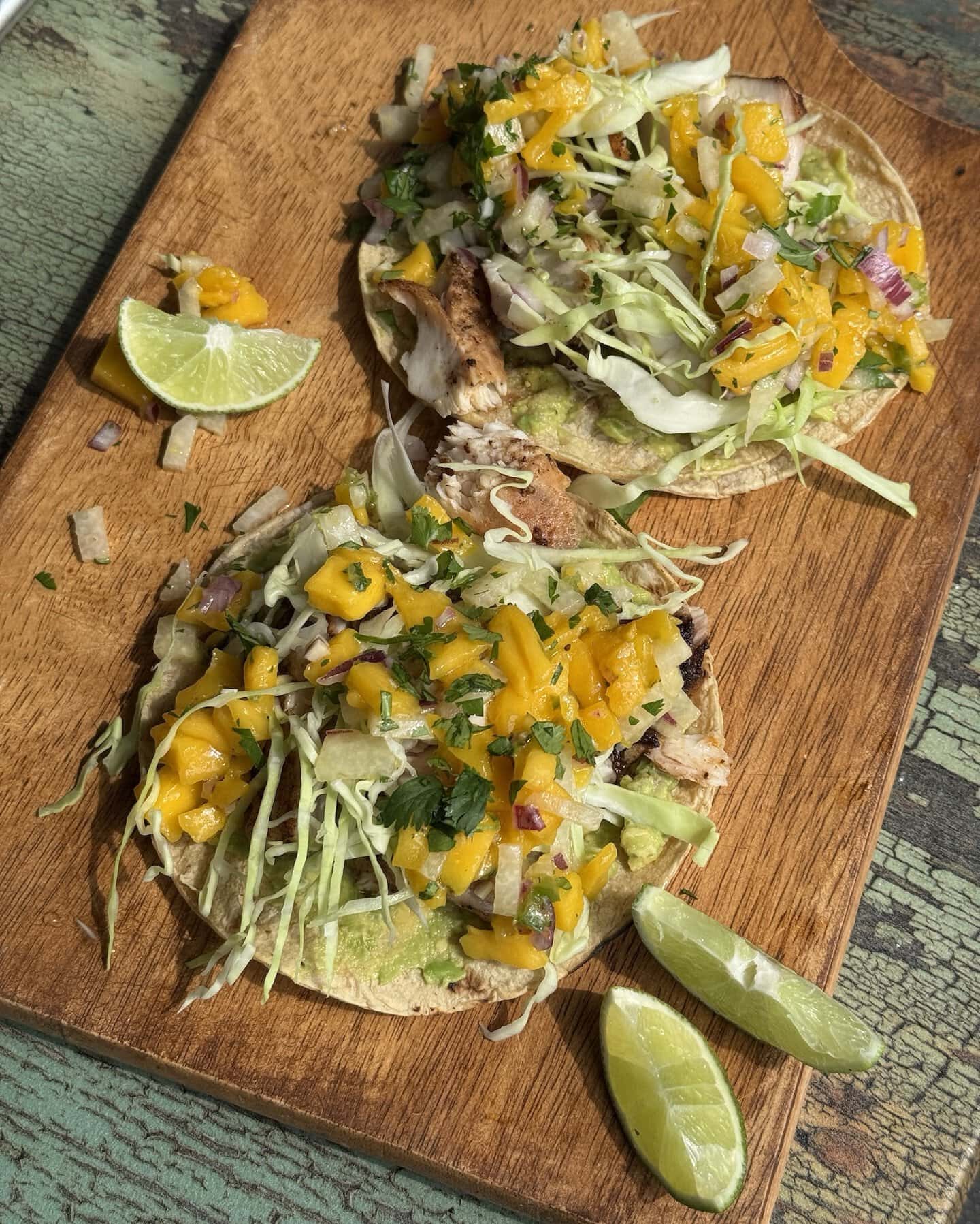two fish tacos with mango salsa on a wooden cutting board with lime wedges