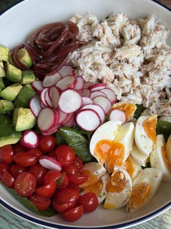 crab marinated red onions cubed avocado sliced radishes jammy eggs and halved cherry tomatoes on a bed of salted lettuce in a serving bowl