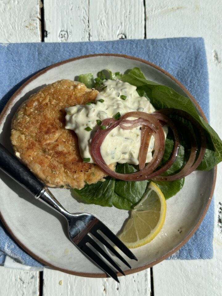 salmon burger on white plate blue napkin topped with tartar sauce
