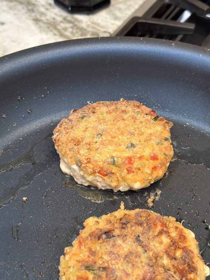 two salmon burger patties in pan cooking