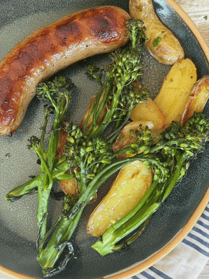 sheet pan sausage and potatoes with broccolini on a blue plate