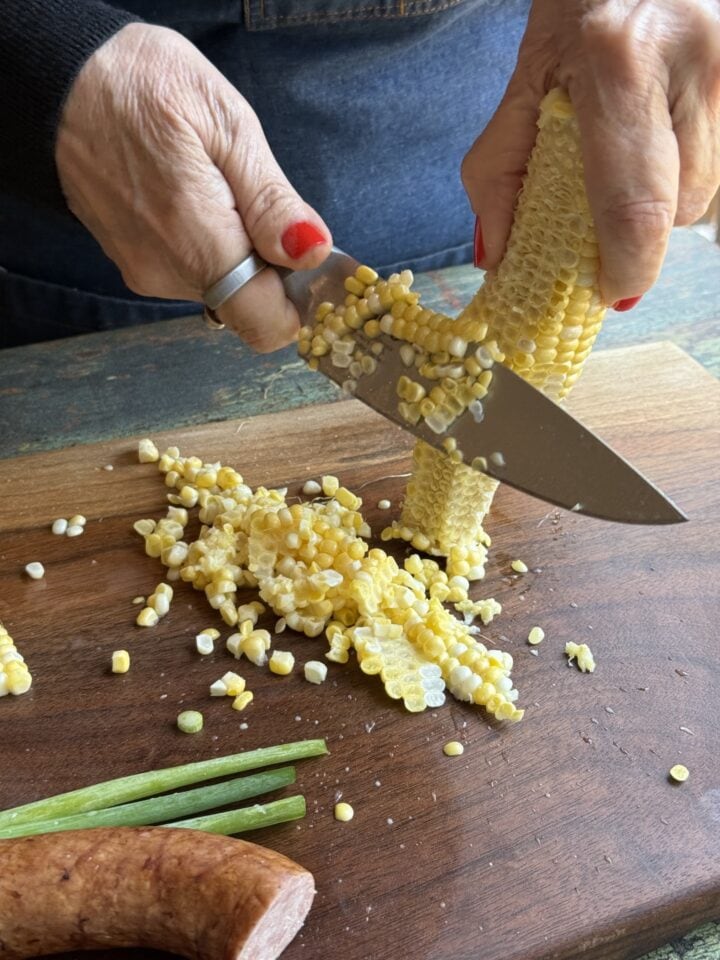 teri cutting corn off the cob on a wooden cutting board