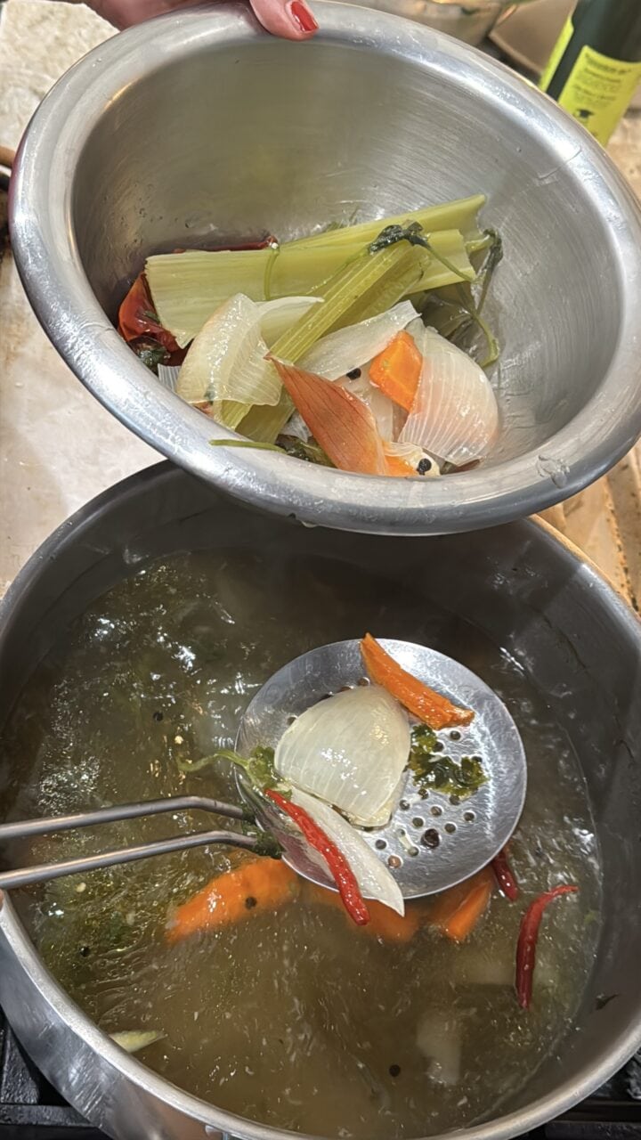 a photo of teri straining the vegetables out of the spicy chicken stock