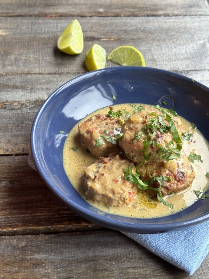 bowl of chicken meatballs in green curry with lime slices next to it