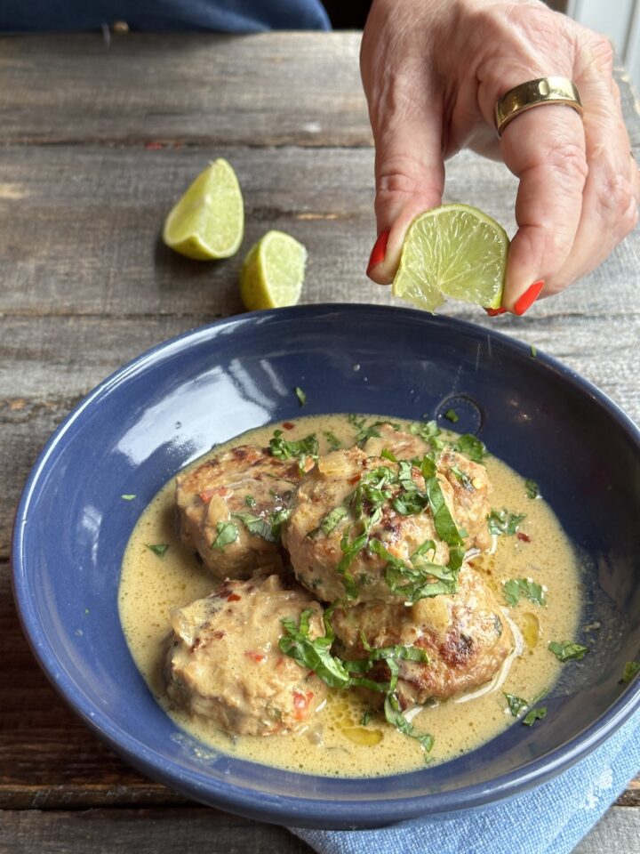 hand squeezing a lime wedge into bowl of curry with chicken meatballs