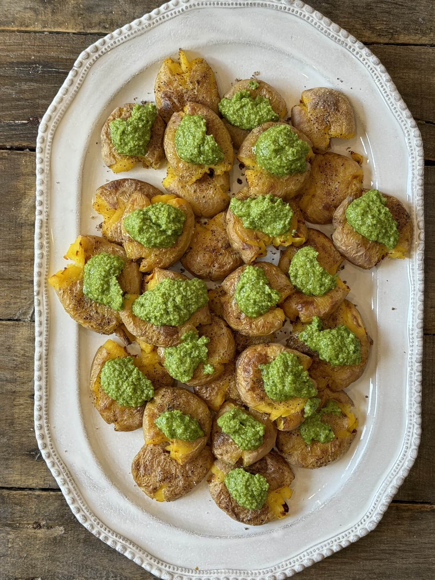 an above view photo of smashed potatoes on a white platter with pesto dolloped on top