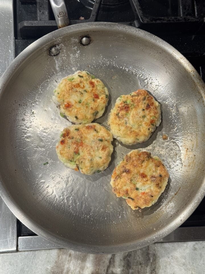 white fish cakes cooking in a stainless steel pan