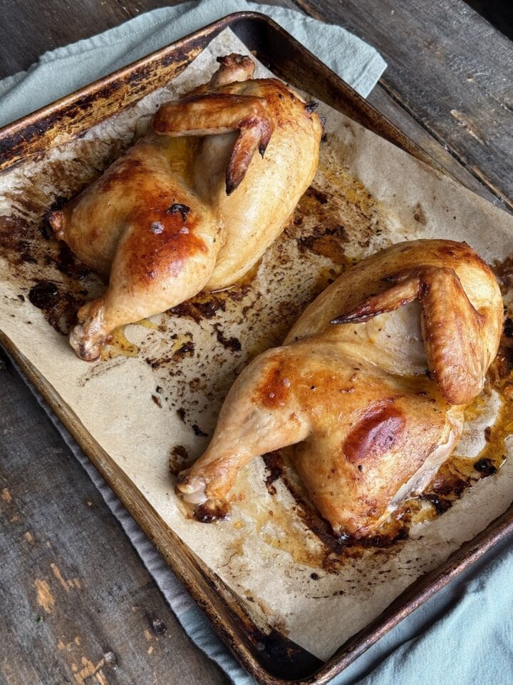 two cooked chicken halves on a baking sheet