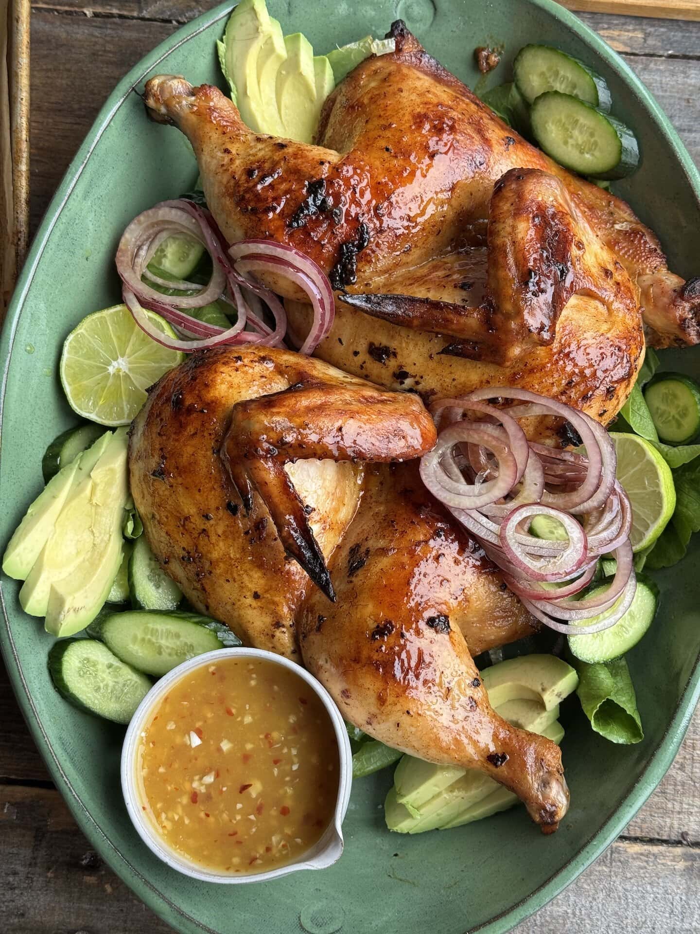 bangkok chicken on a bed of greens with a small bowl of mango chili sauce