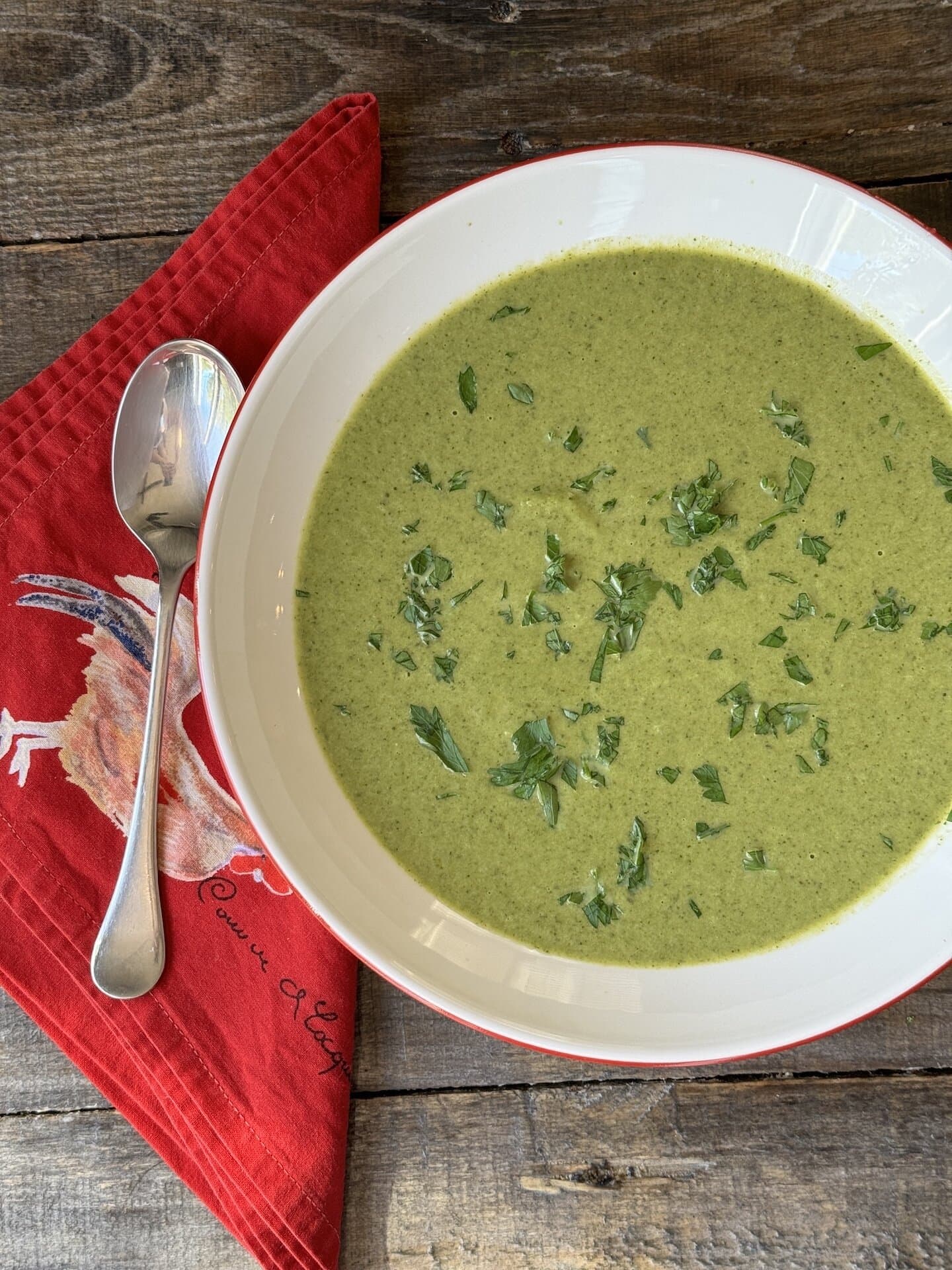 a photo of broccolini soup in a bowl with basil on top and a spoon next to it