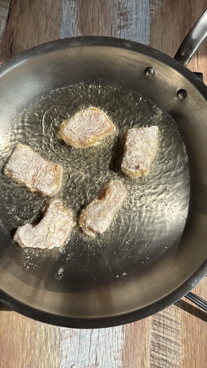 chicken bites frying in a stainless steel pan