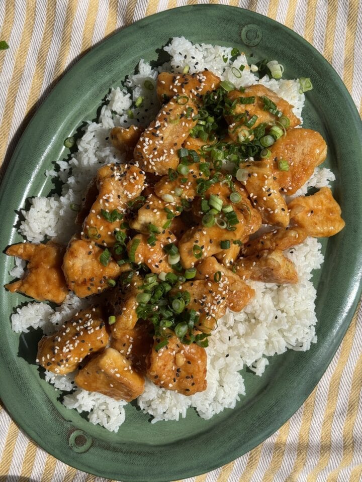 easy orange chicken on a bed of white rice on a green platter