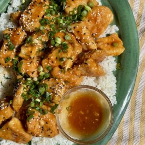 orange chicken on a bed of rice on a green platter