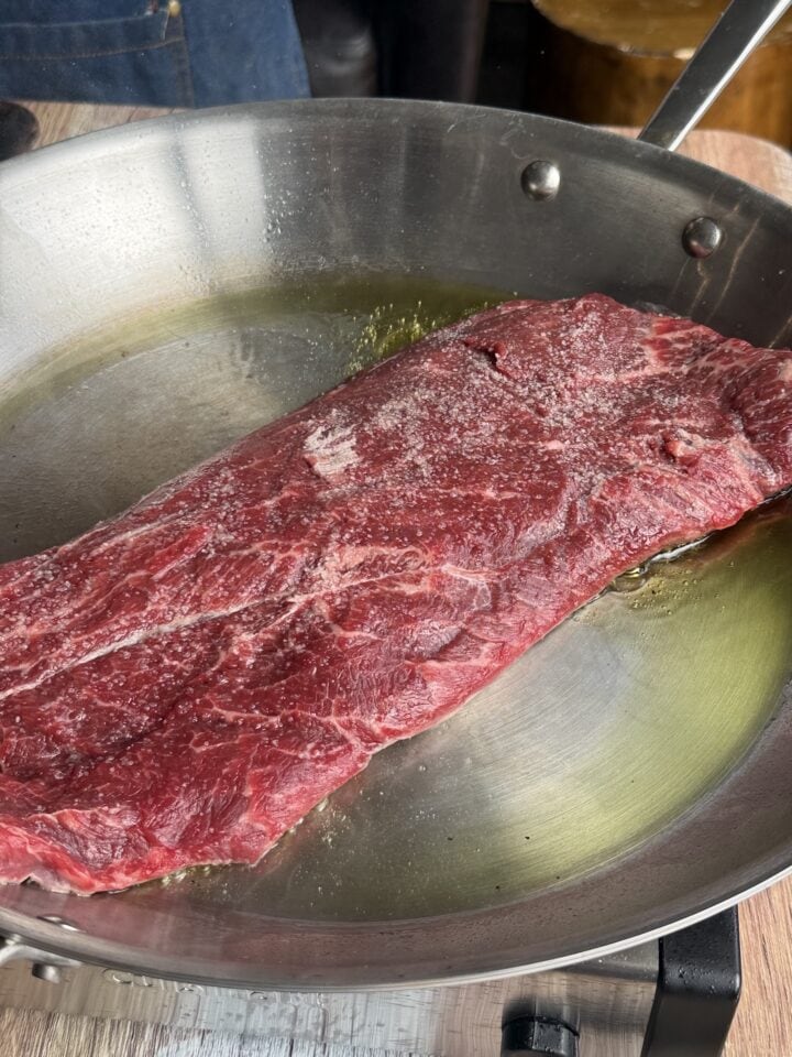 flat iron steak cooking in a stainless steel pan