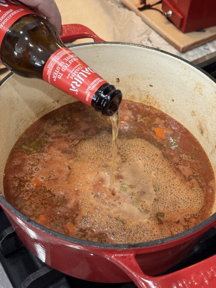 beer pouring into a dutch oven with pot roast liquids