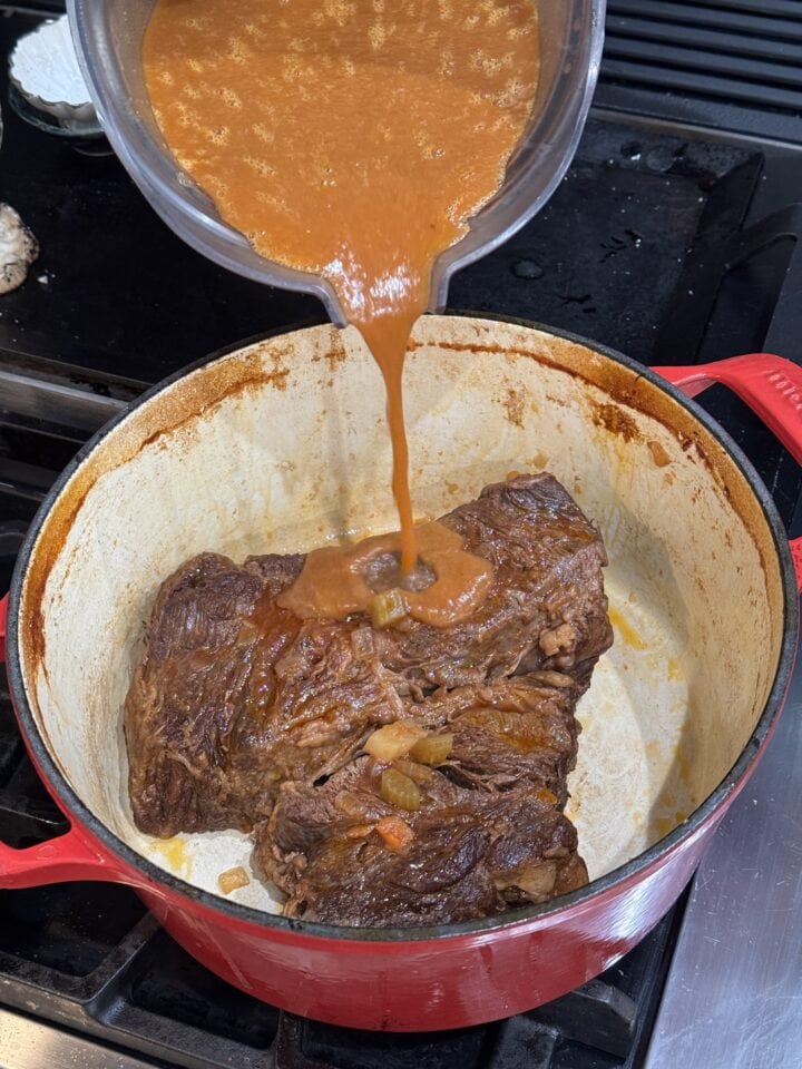 pouring pureed liquid on top of the pot roast in a dutch oven