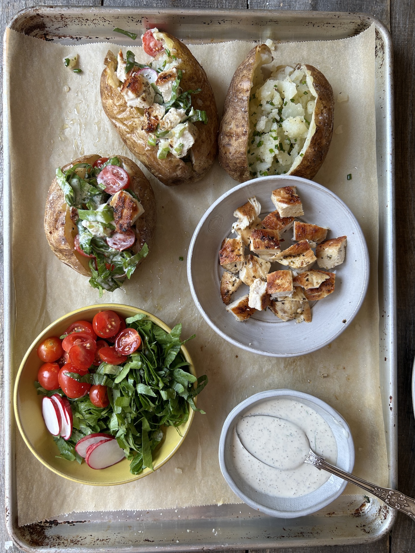 a photo of stuffed potatoes on a sheet tray with chicken and toppings in bowls