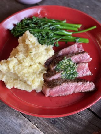 sliced ribeye and mashed potatoes on a red plate