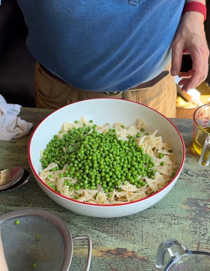 peas on top of farfalle pasta in a large serving bowl