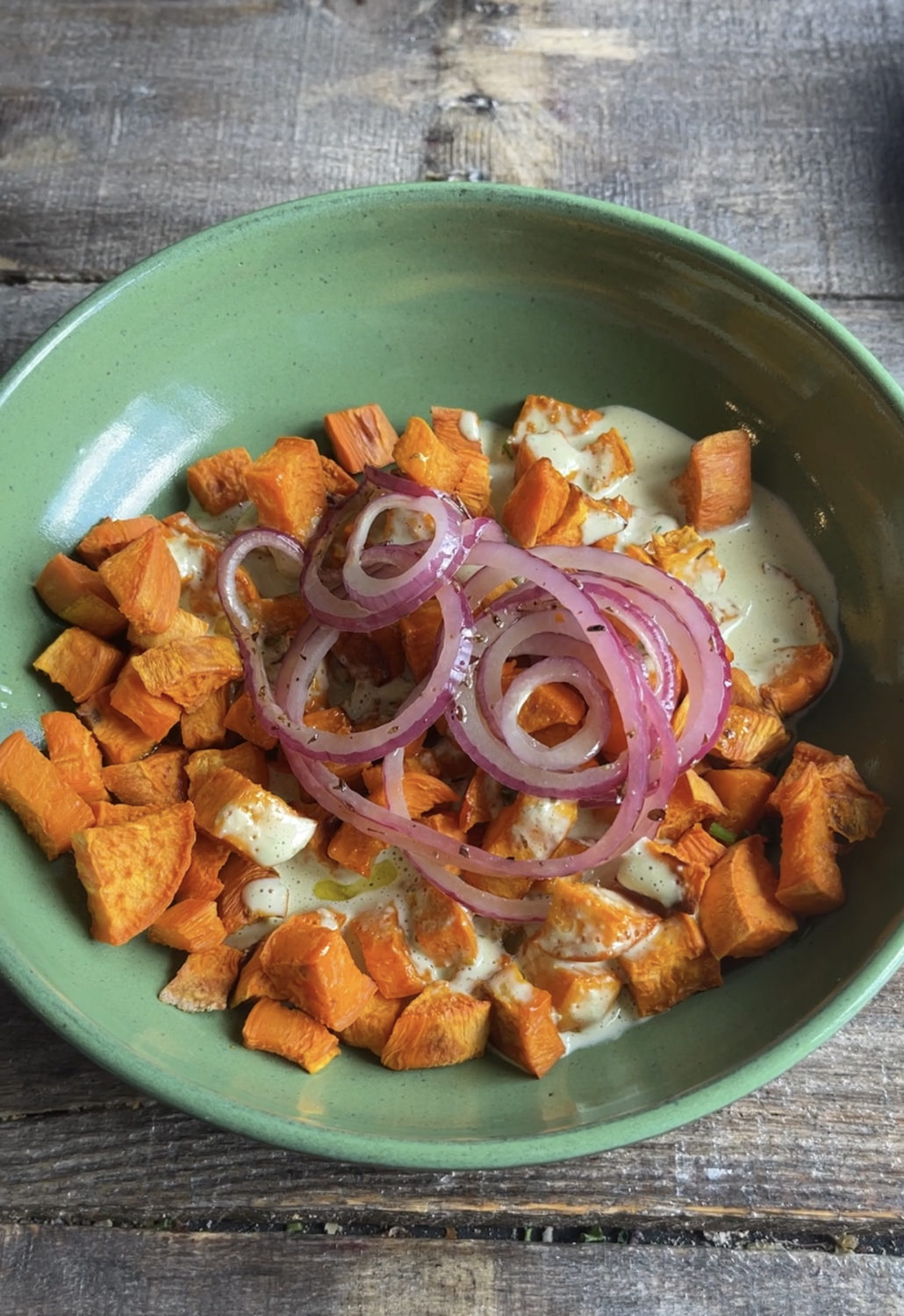 sweet potato cubes in a green bowl with onions and dressing
