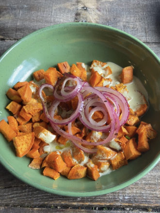 sweet potato cubes in a green bowl with onions and dressing