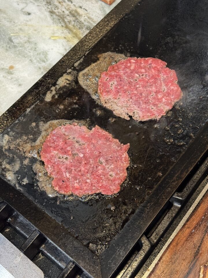 two smashburger patties cooking on a griddle pan