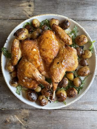 brick chicken on a white platter with potatoes and greens