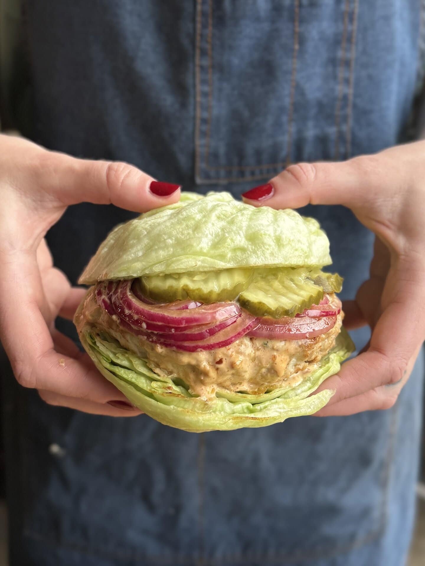 a photo of hands holding a ground chicken burger on a lettuce bun