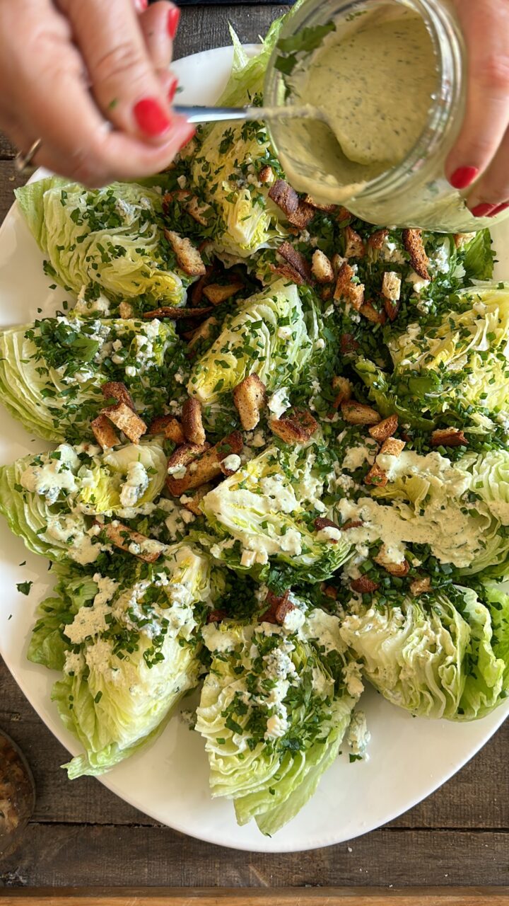 A wedge salad being dressed with creamy olive dressing.