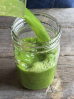 Green juice being poured into a mason jar.