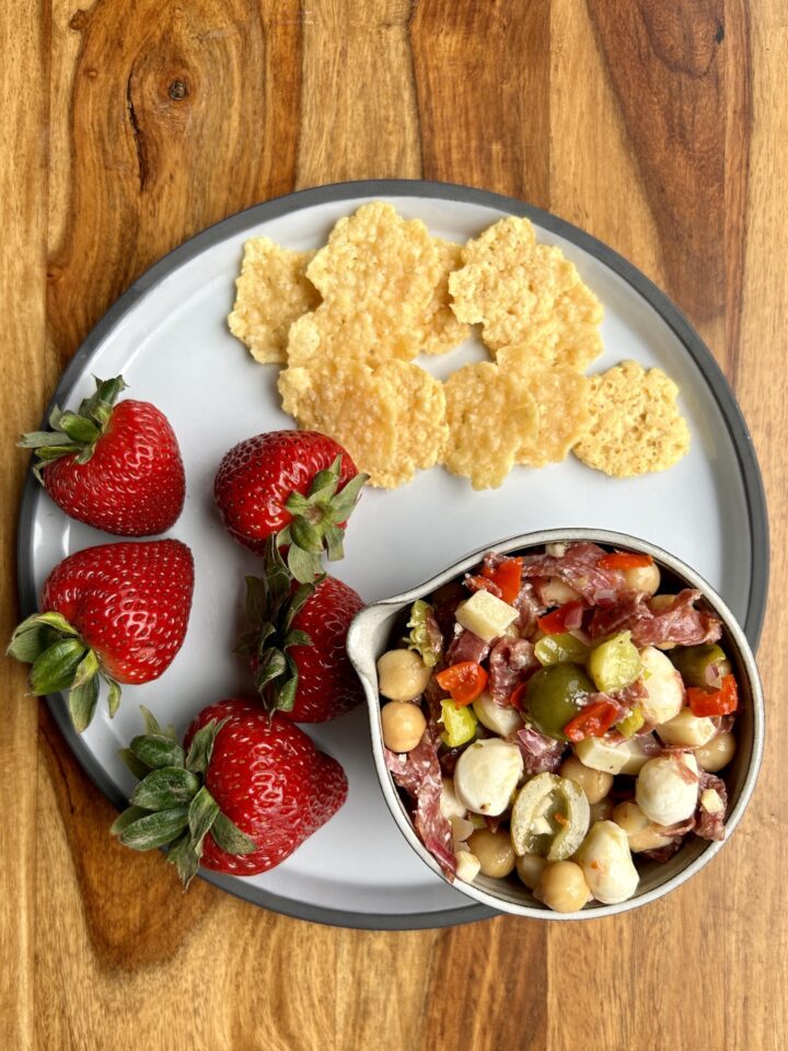 white plate a bowl of grinder salad, strawberries, & crisps.