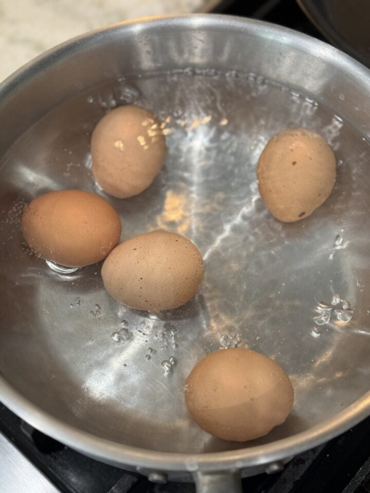 Boiled eggs in a stainless steel pan, ready for cooking or recipe preparation.
