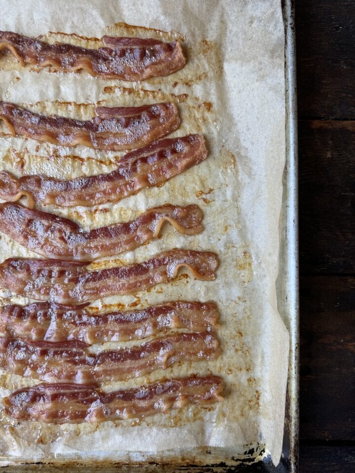 Bacon strips on parchment paper, close-up view of crispy cooked bacon for breakfast or recipe ideas.