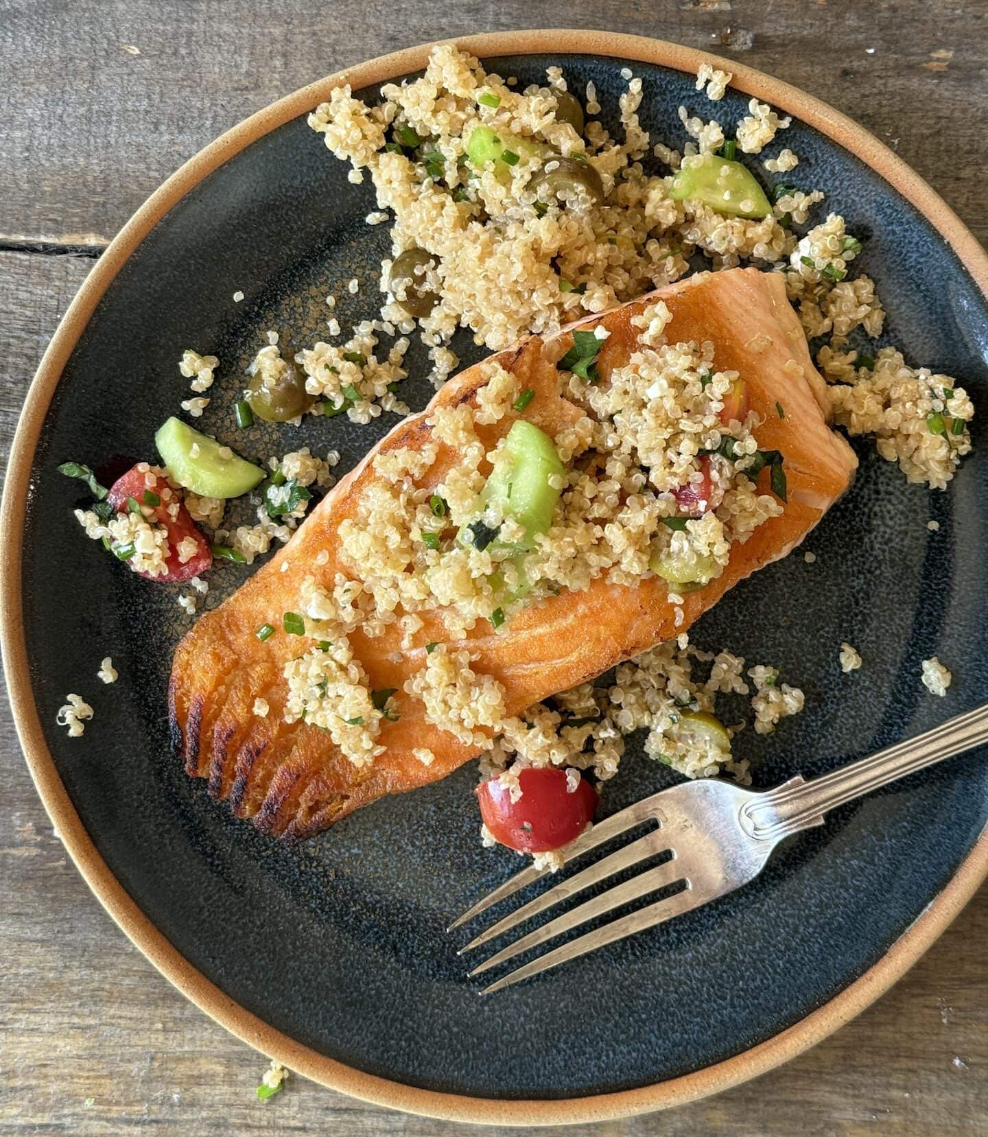 an above view photo of salmon on a blue plate with quinoa salad on top