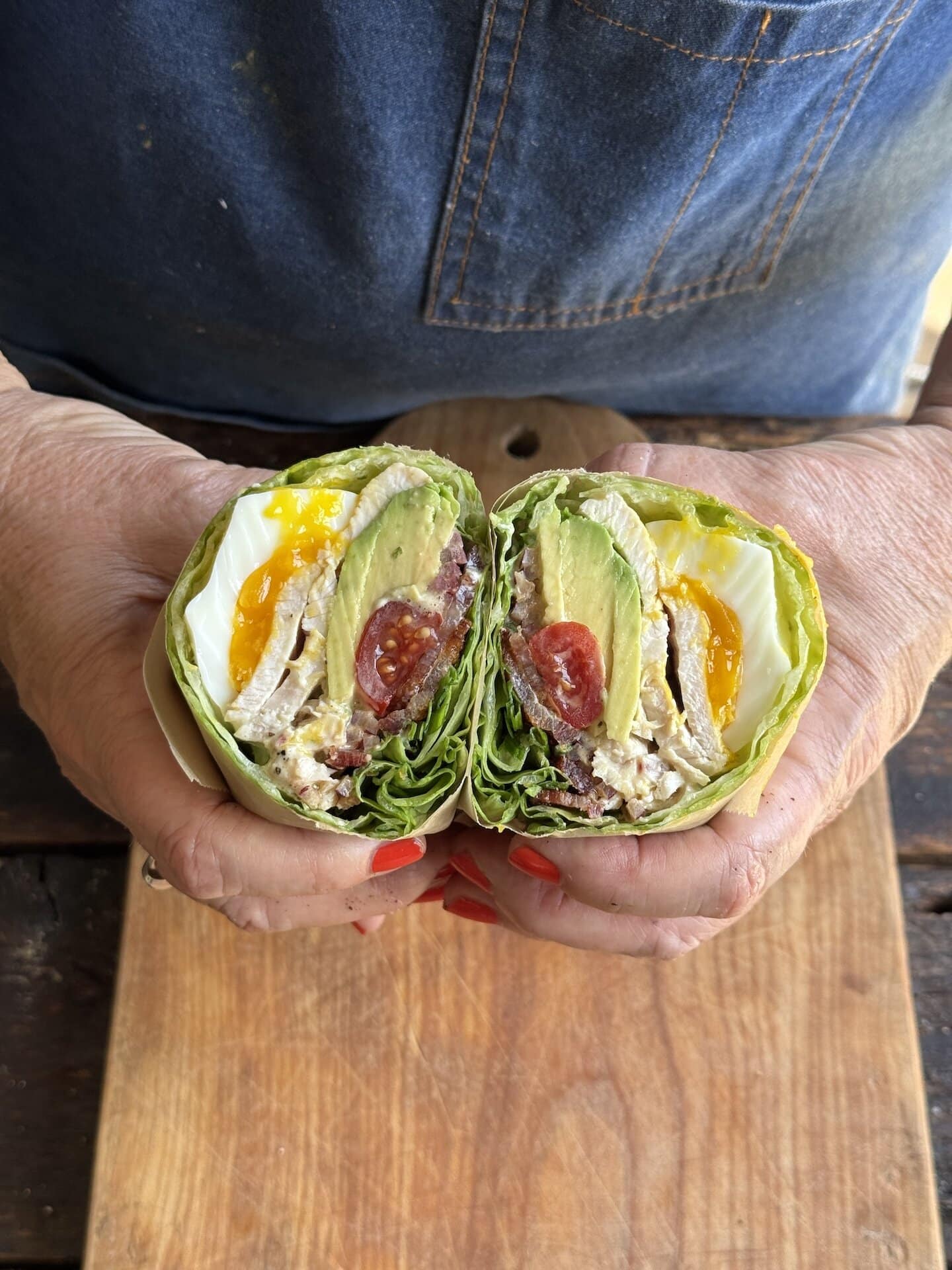 chicken bacon wrap cut in half being held in two hands by person with blue apron
