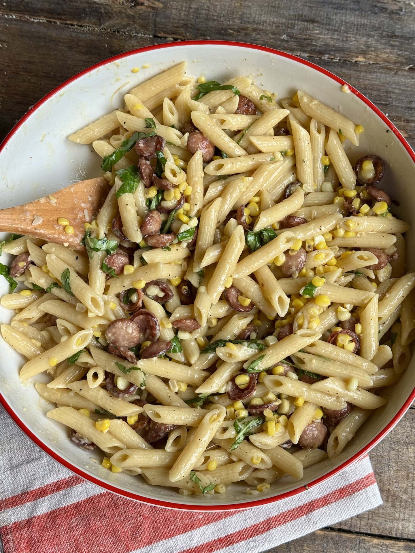 a photo of corn pasta with sausage in a large bowl with a wooden spoon in it