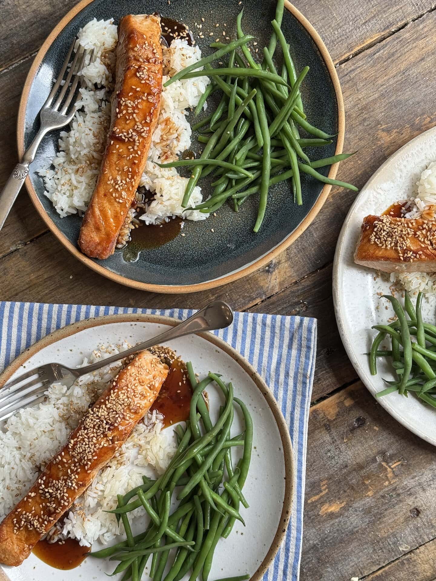 a photo of three plates with teriyaki glazed salmon, rice and green beans