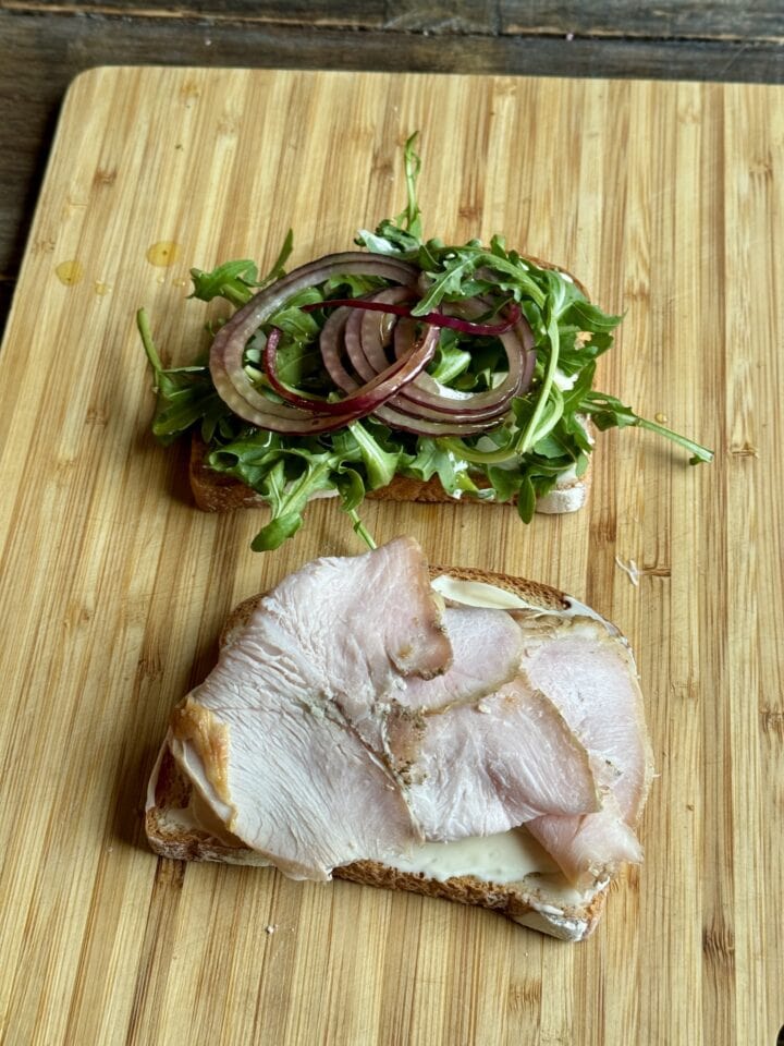 a photo of a sandwich open face with greens and marinated onions on one side and turkey on the other