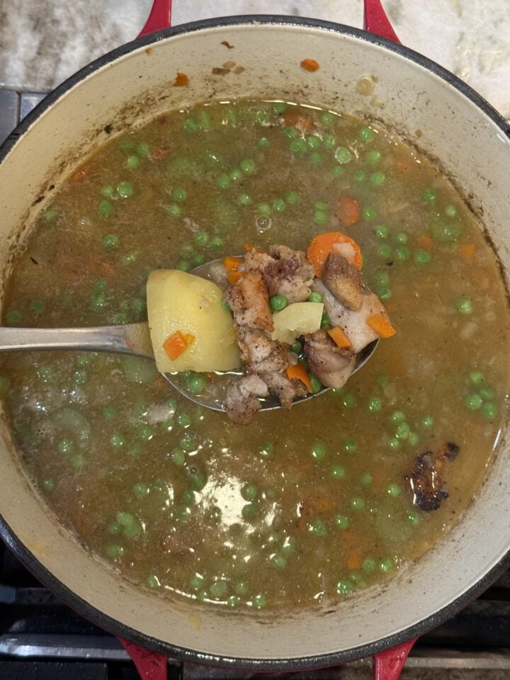 a photo of potato soup with chicken on a spoon above a soup pot