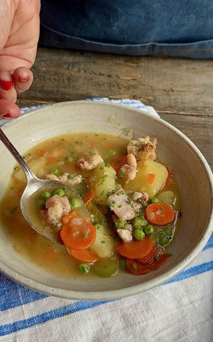 hand holding spoonful of soup from a white bowl on a stripped napkin