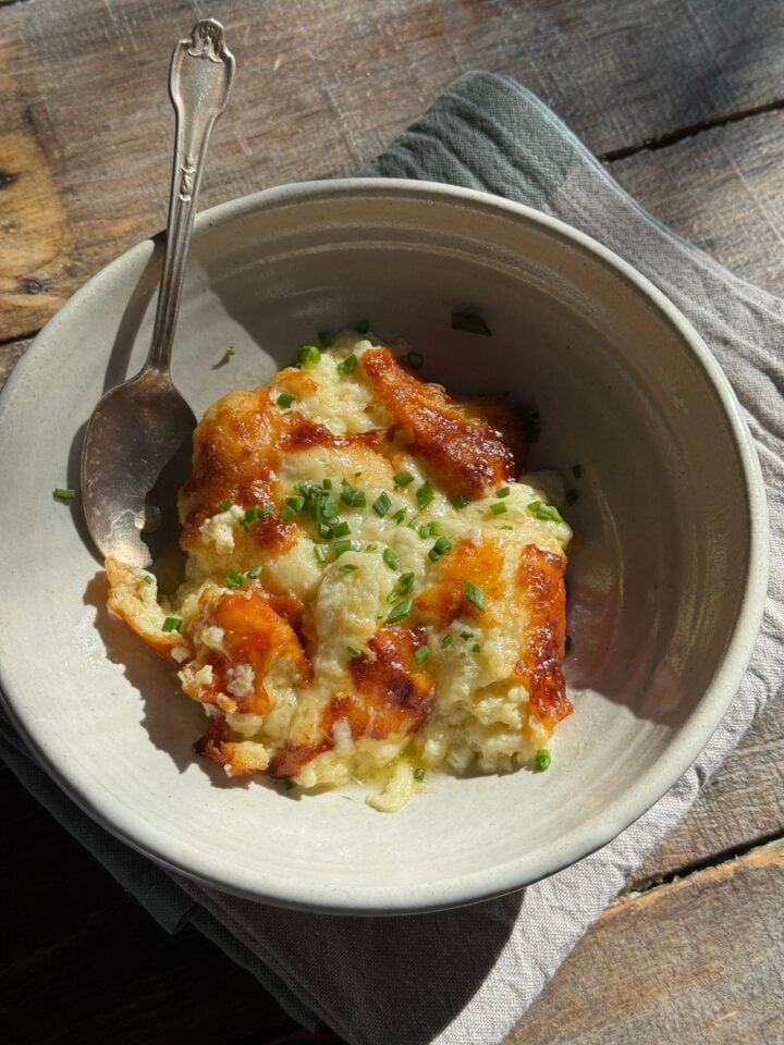 a piece of cheese souffle in a bowl with chives on top and a spoon in it
