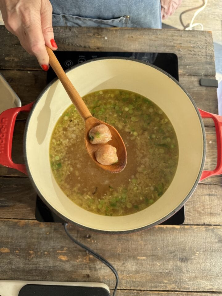 meatballs on a wooden spoon above the chicken soup in a dutch oven