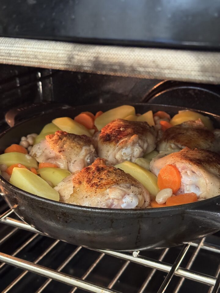 chicken thighs with potatoes in a cast iron skillet in the oven