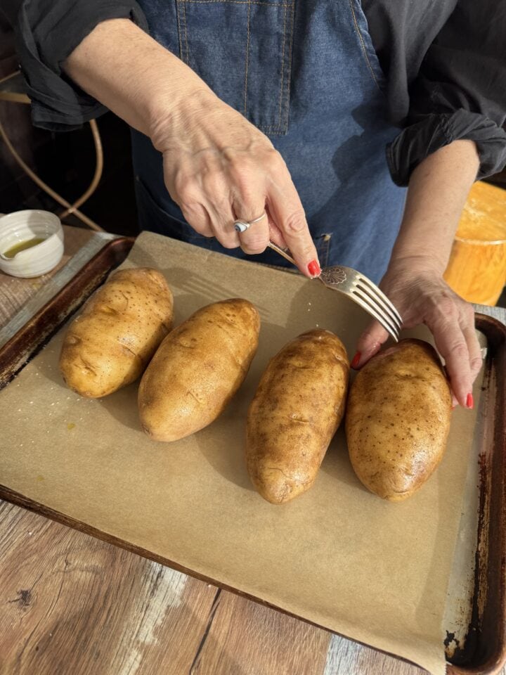 teri poking baked potatoes with a fork on a baking sheet